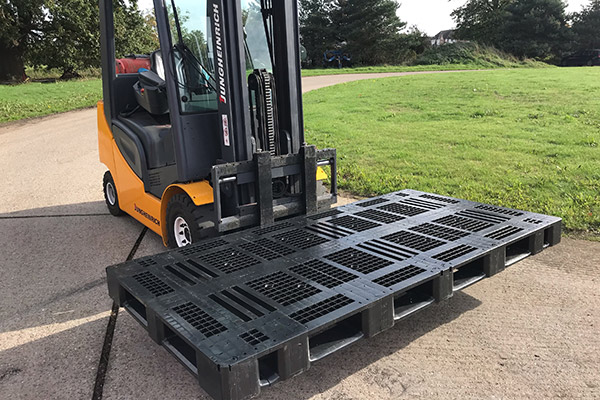 An oversize plastic pallet being moved by a forklift truck.
